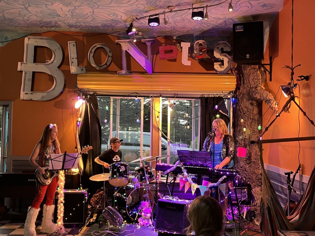 three of the four band members playing in front of a window at Blondie's